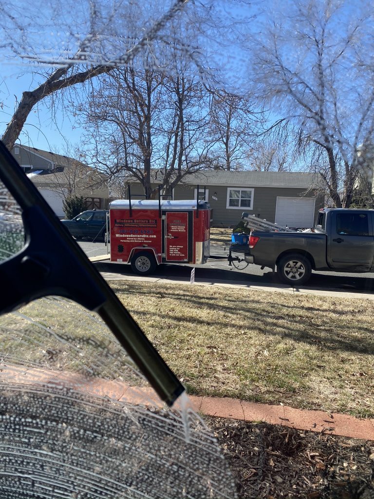 Window cleaning with a squeegee and Winodws Gutters Etc Trailer in the background